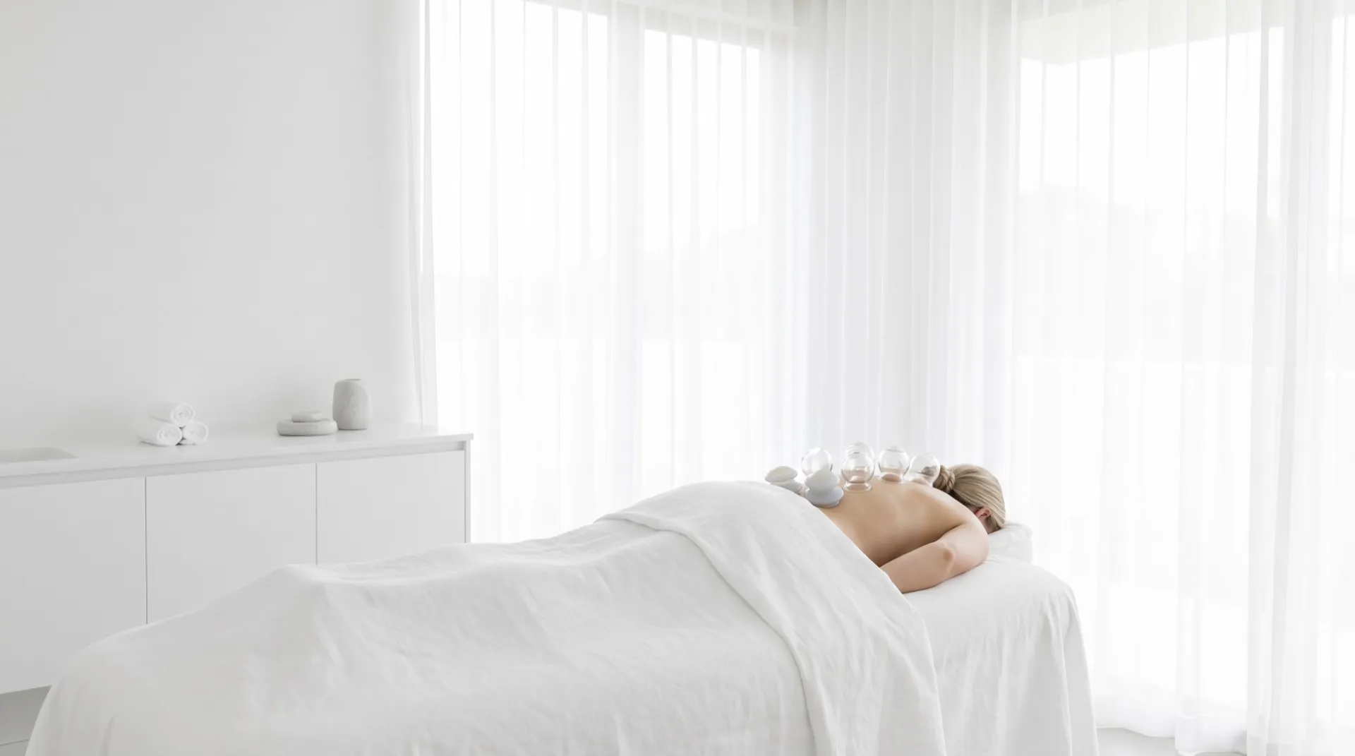 Client resting face down under a white sheet in a bright treatment room