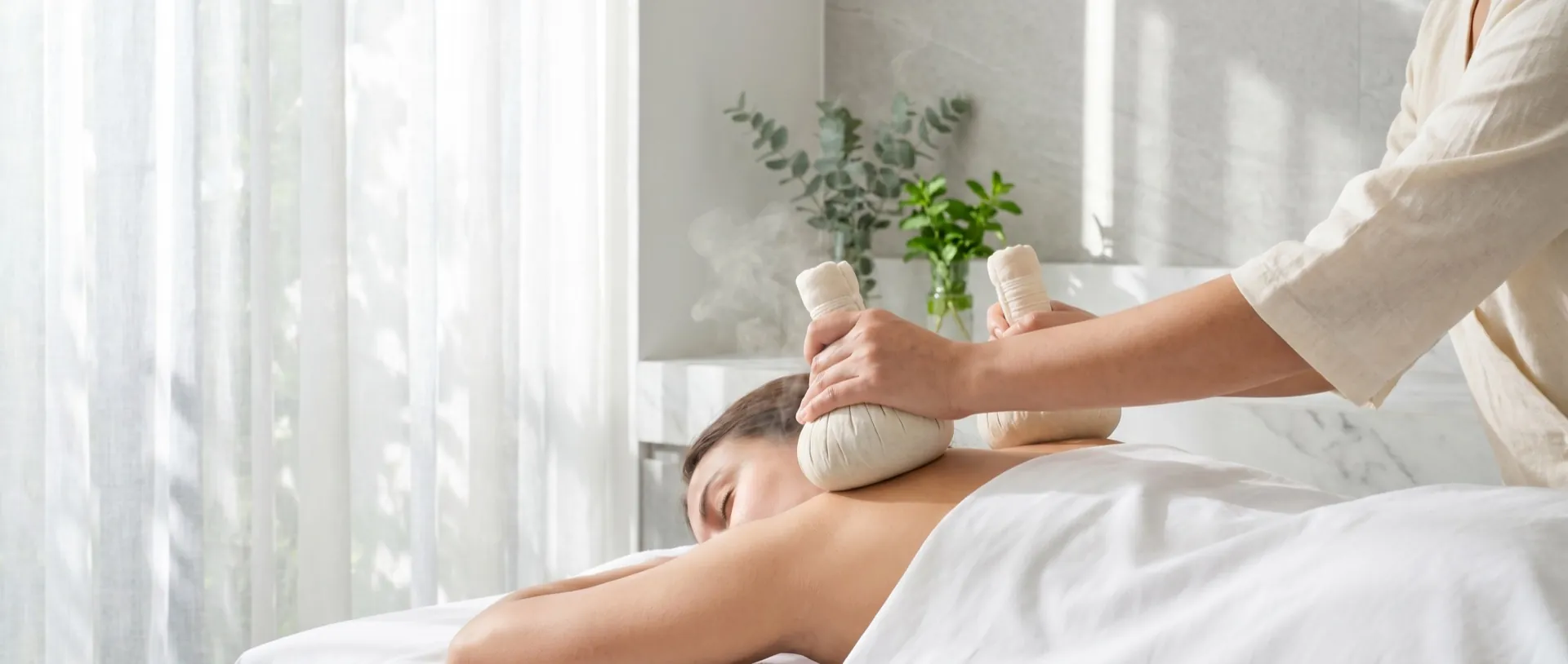 Warm herbal compresses applied to a client's shoulders during a Thai stem massage