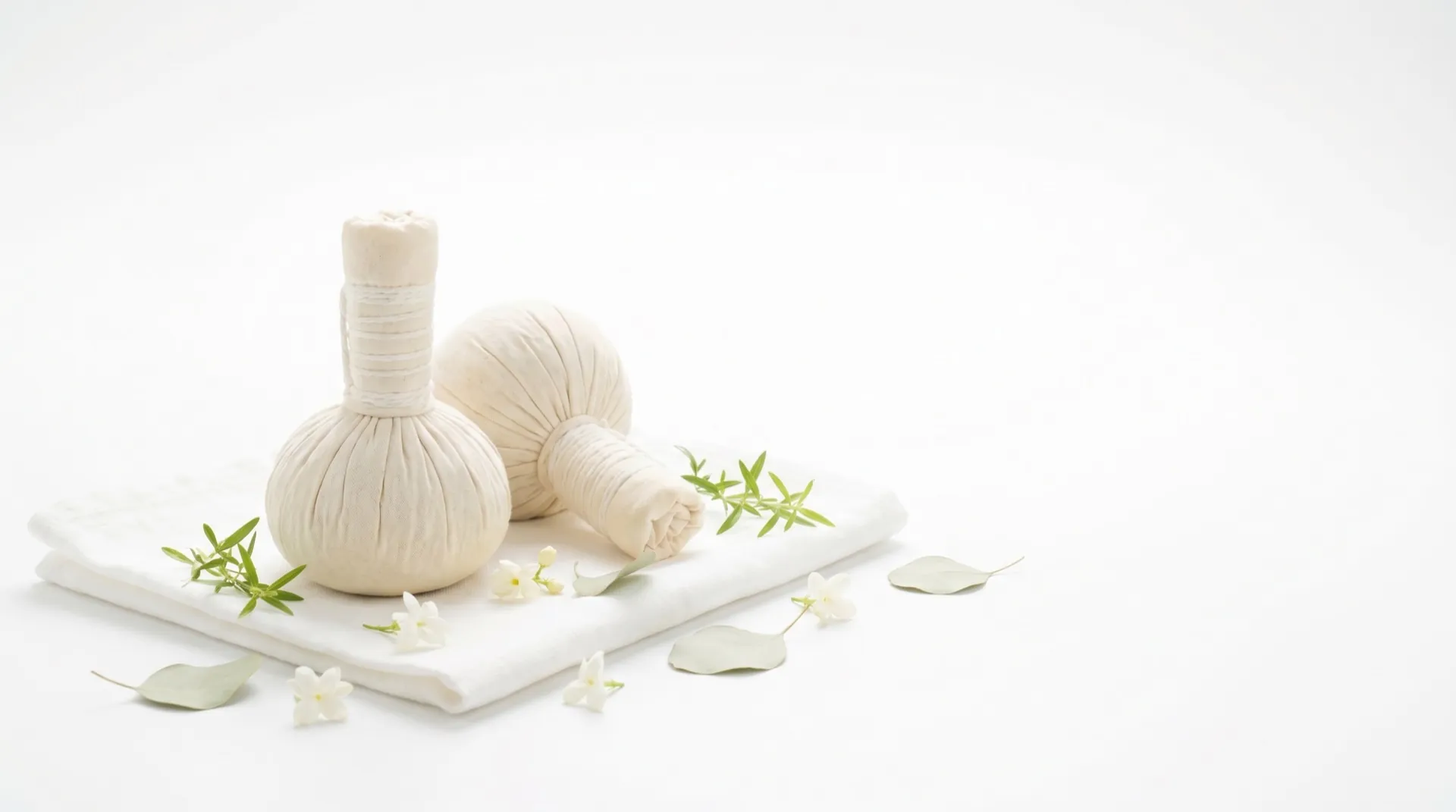 Thai herbal compress balls on a folded towel with fresh herbs